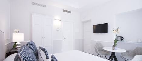 A hotel room with a large bed, two chairs, a small table, a TV, and a coffee machine.