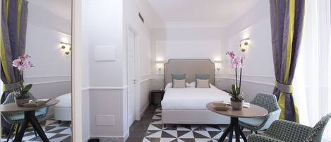 Una habitación de hotel con cama, dos sillas, una mesita pequeña y una orquídea en maceta.