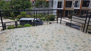 Une terrasse sur le toit, dotée d’un sol carrelé et entourée d’une rambarde en métal, d’où l’on peut admirer une rue bordée de voitures garées et d’immeubles.