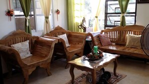 Un salon chaleureux, doté de meubles en bois, notamment deux fauteuils et un canapé, d’une table basse en verre et d’un ventilateur.