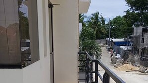 Un balcon étroit doté d’un sol carrelé, d’une rambarde noire et offrant une vue sur une rue où des travaux de construction sont en cours.