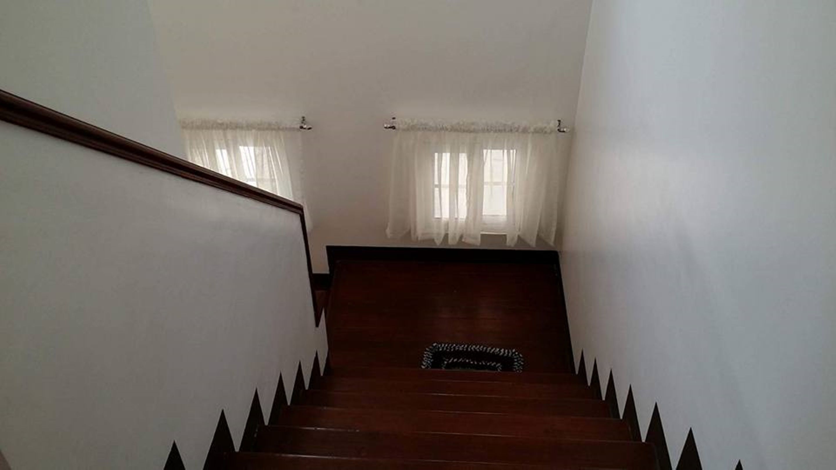 A staircase with wooden steps and black-tipped edges, leading to a landing with a black rug.