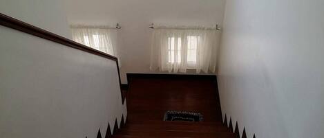 A staircase with wooden steps and black-tipped edges, leading to a landing with a black rug.