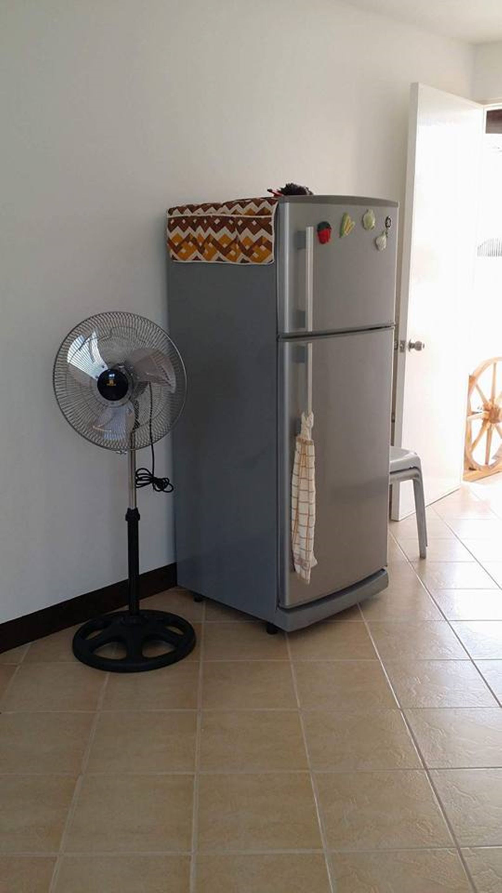 Una cocina pequeña con refrigerador, ventilador y un taburete.