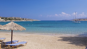 A beach with clear blue water, a boat in the distance, and a straw umbrella. - Villa Olea Prime (Chania)