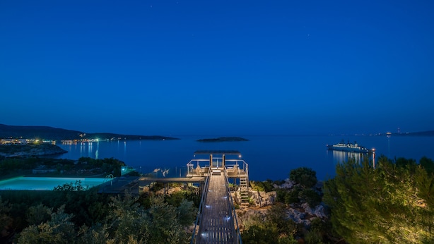A waterfront property with a wooden deck leading to a covered area with seating, overlooking a calm sea and distant shoreline. - Villa Olea Prime (Chania)