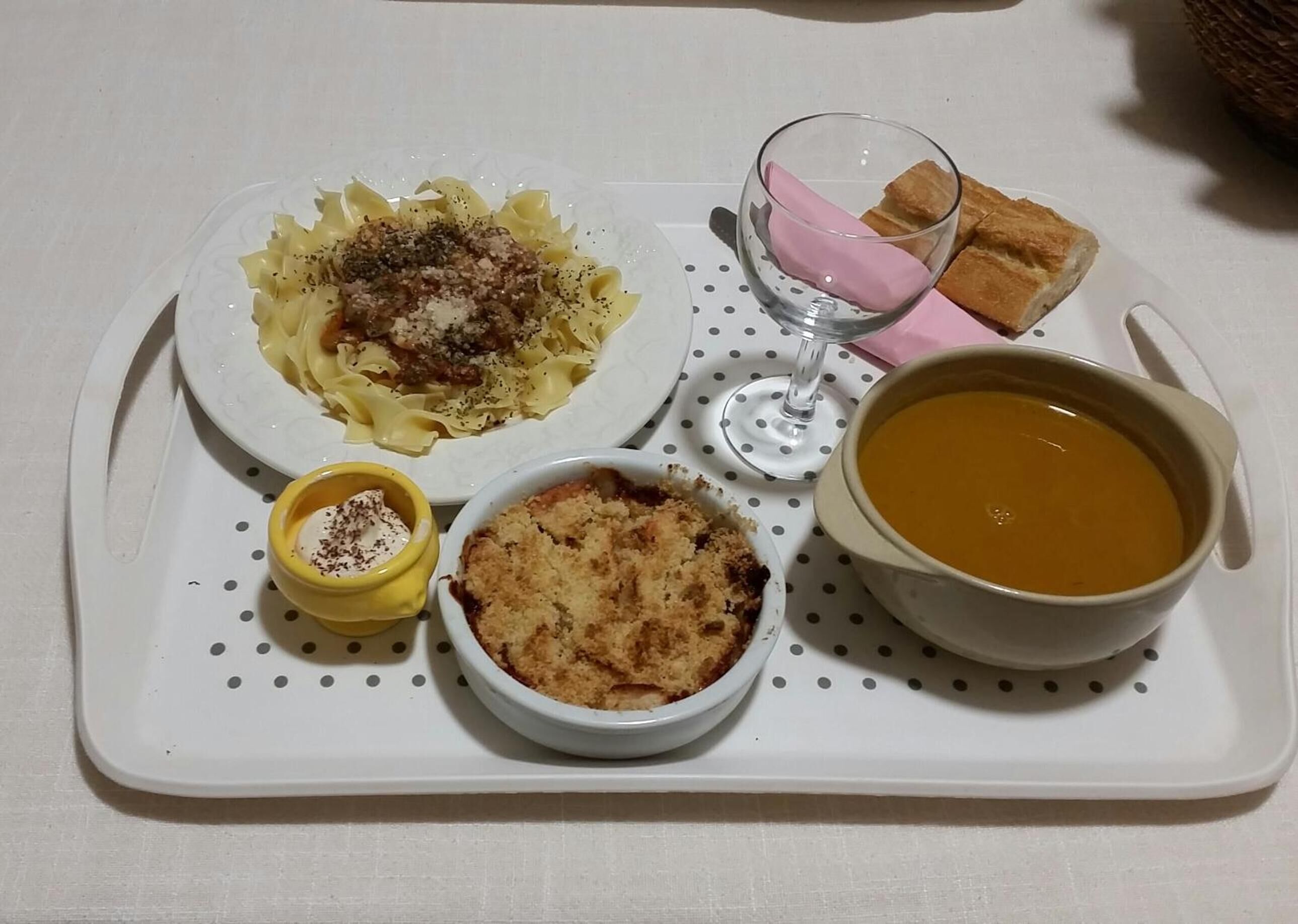 A tray with pasta, a bowl of soup, a dessert, and a glass of wine.