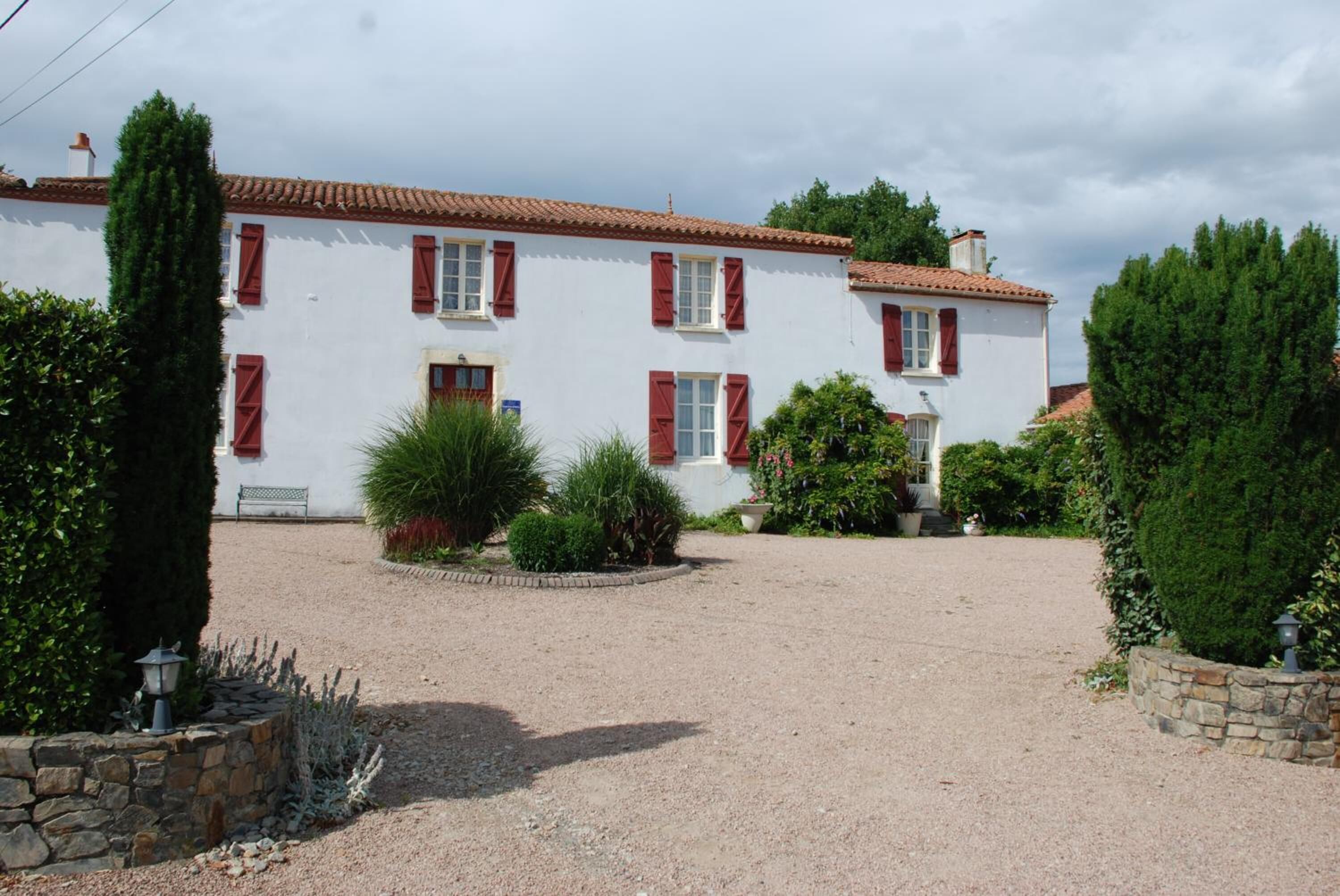 Un bâtiment à deux étages avec des volets rouges et une allée gravillonnée.