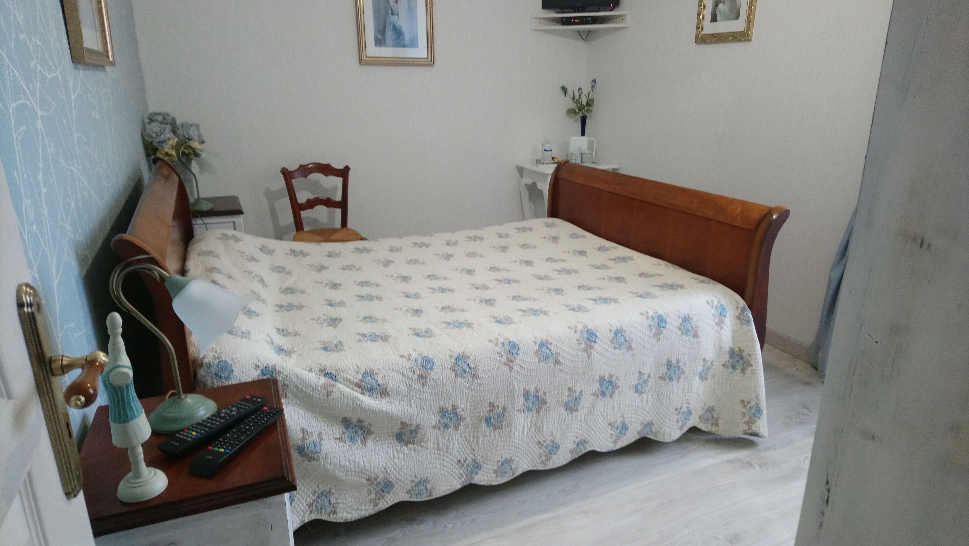 Ein Schlafzimmer mit Bett, Sessel, Nachttisch, Lampe und einem kleinen Tisch mit Fernbedienung.