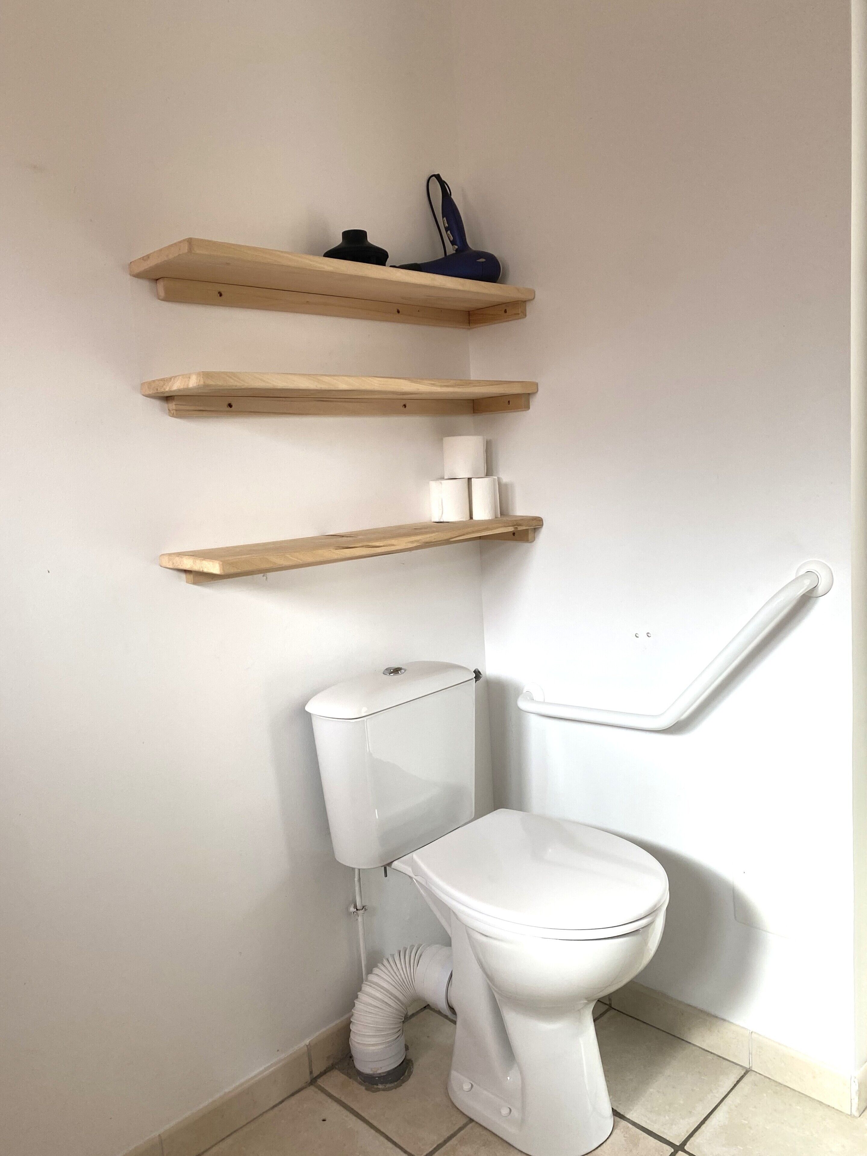 Un baño con inodoro, un sujetapapeles blanco y tres estantes de madera.