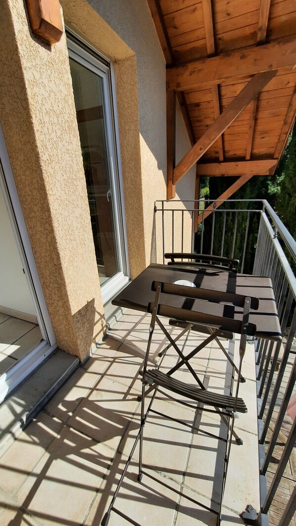 Un balcón con una mesa y sillas de metal, techo de madera y puerta de cristal.