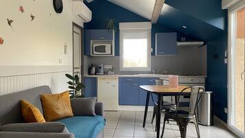 A compact kitchen with a dining area, a sofa, and a potted plant.