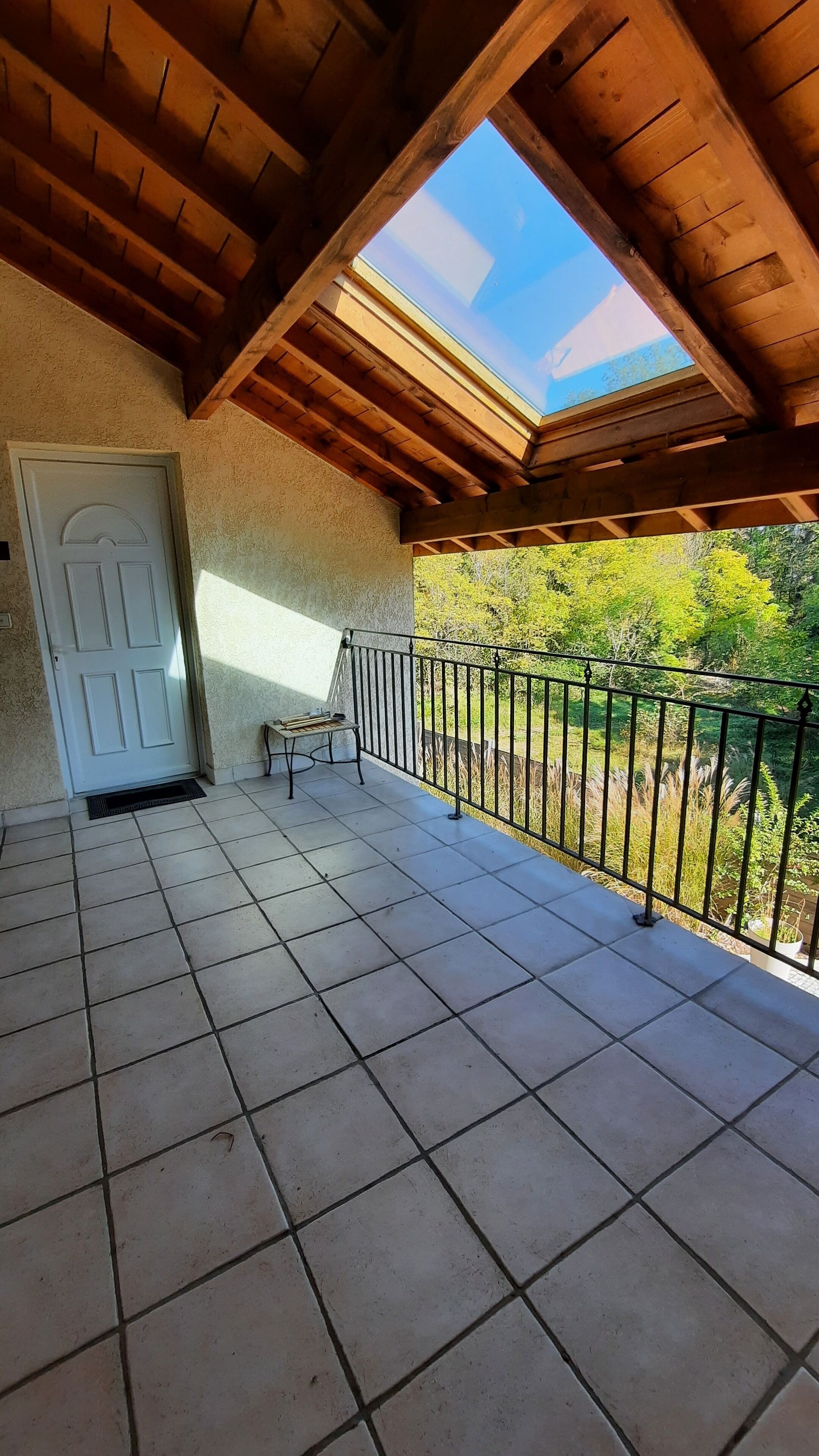 A covered balcony with a wooden ceiling and a view of greenery.