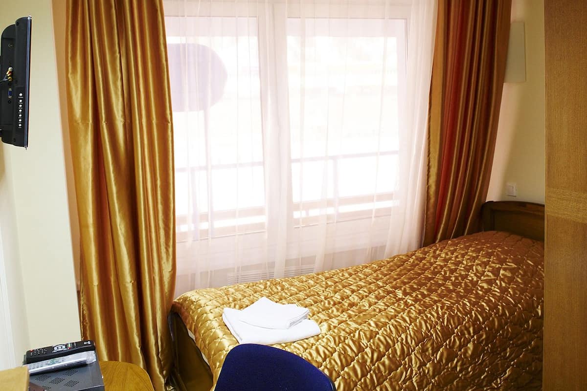 A hotel room with a bed, a desk with a telephone, a chair, and a window with curtains.
