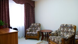 A living room with a wooden desk, two floral armchairs, a small round table, and a potted plant.