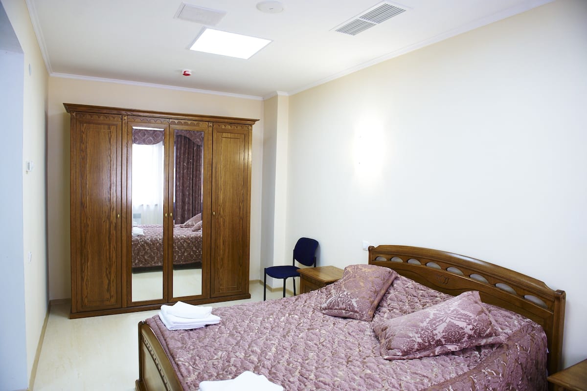 A bedroom with a bed, a wooden wardrobe, a chair, and a desk.