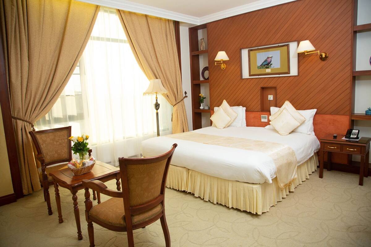 A hotel room with a large bed, a desk with a chair, a lamp, and a picture on the wall.