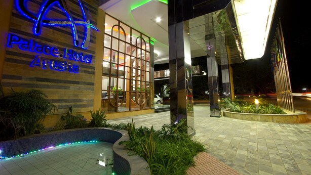 Eksteriøret af Palace Hotel Arusha, med en moderne facade, et markant neon-skilt, en glasindgang og et anlagt poolområde.