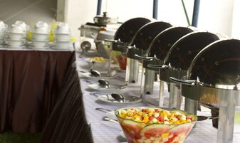 Montaje de bufé con varios dispensadores de alimentos y un tazón grande de ensalada de frutas.