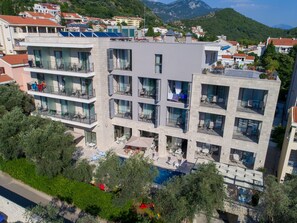 A multi-story hotel with balconies, a swimming pool, and a view of the surrounding town and mountains. - Hotel Eleven (Petrovac)