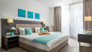 Une chambre d’hôtel moderne avec un grand lit, deux tables de chevet, un bureau et une fenêtre avec des rideaux.