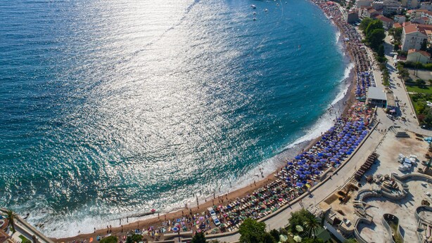 Une ville côtière dotée d’une plage bordée de parasols et de chaises longues, d’une promenade et de bâtiments le long du littoral.