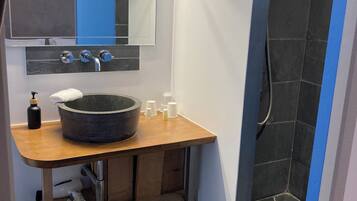 Un baño con tocador de madera, un lavamanos amplio, un espejo y zona de ducha.