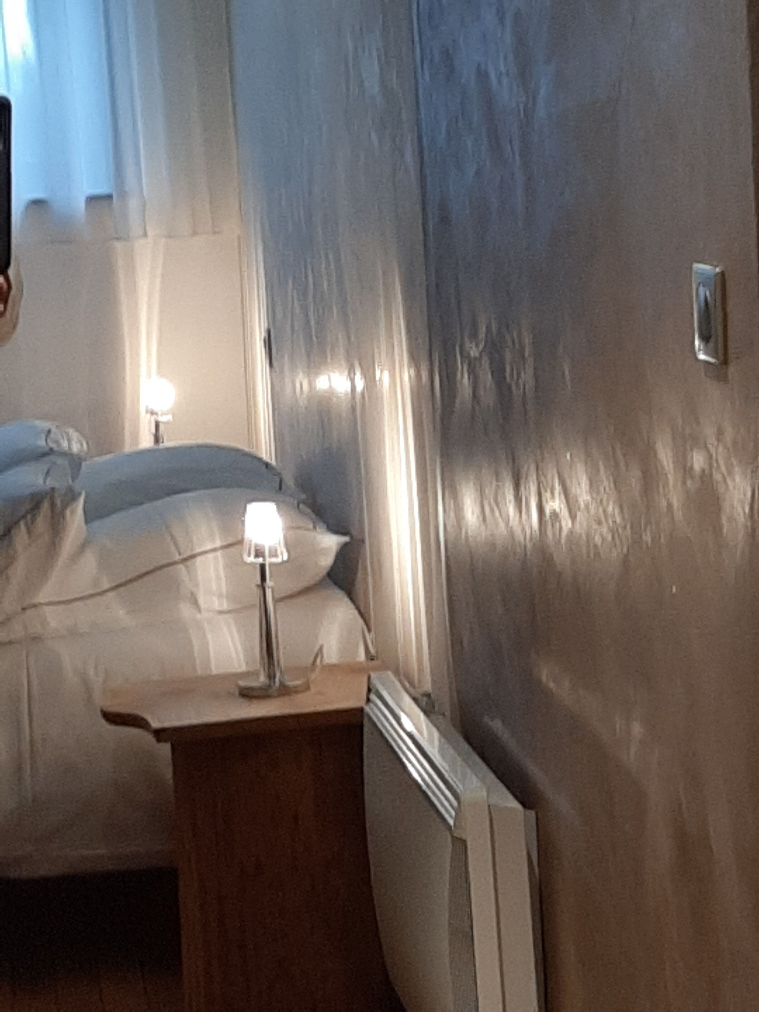 A hotel room with a bed, a nightstand with a lamp, and a radiator.