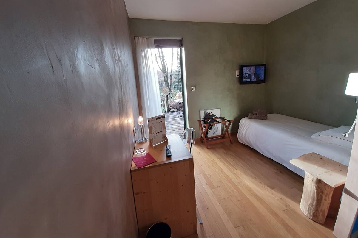 A room with a wooden desk, a bed, a television, and a window with curtains.