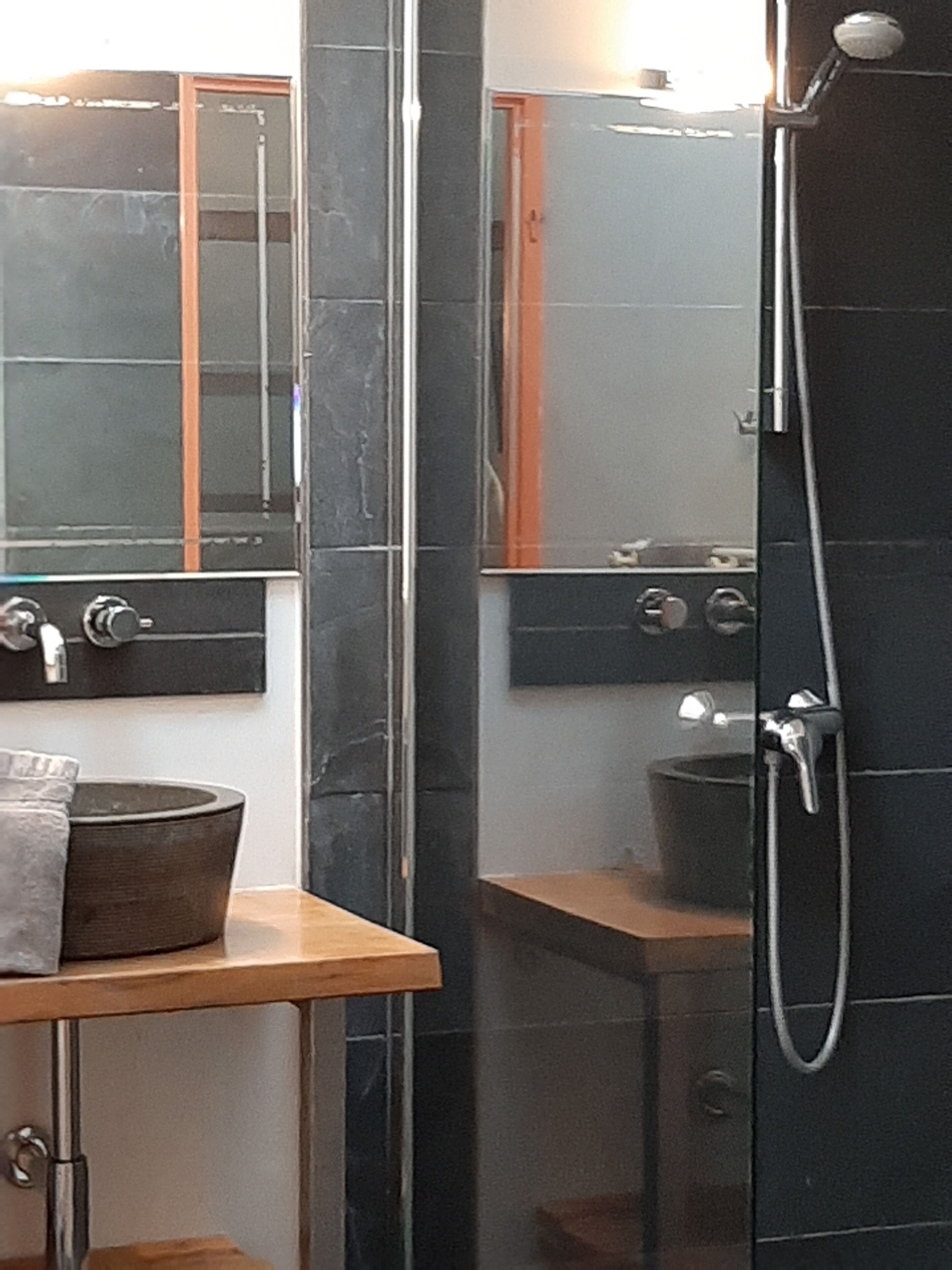 A bathroom with a glass-enclosed shower, a wooden vanity with a bowl sink, and a mirror above the sink.