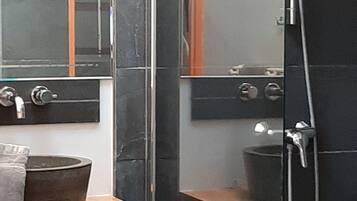 A bathroom with a glass-enclosed shower, a wooden vanity with a bowl sink, and a mirror above the sink.