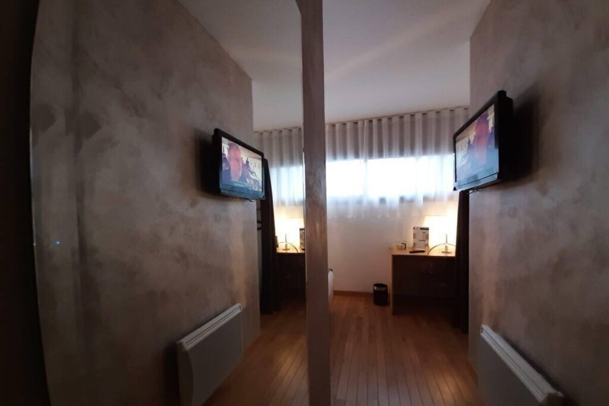 A narrow hallway with wooden flooring, flanked by walls with mounted televisions.