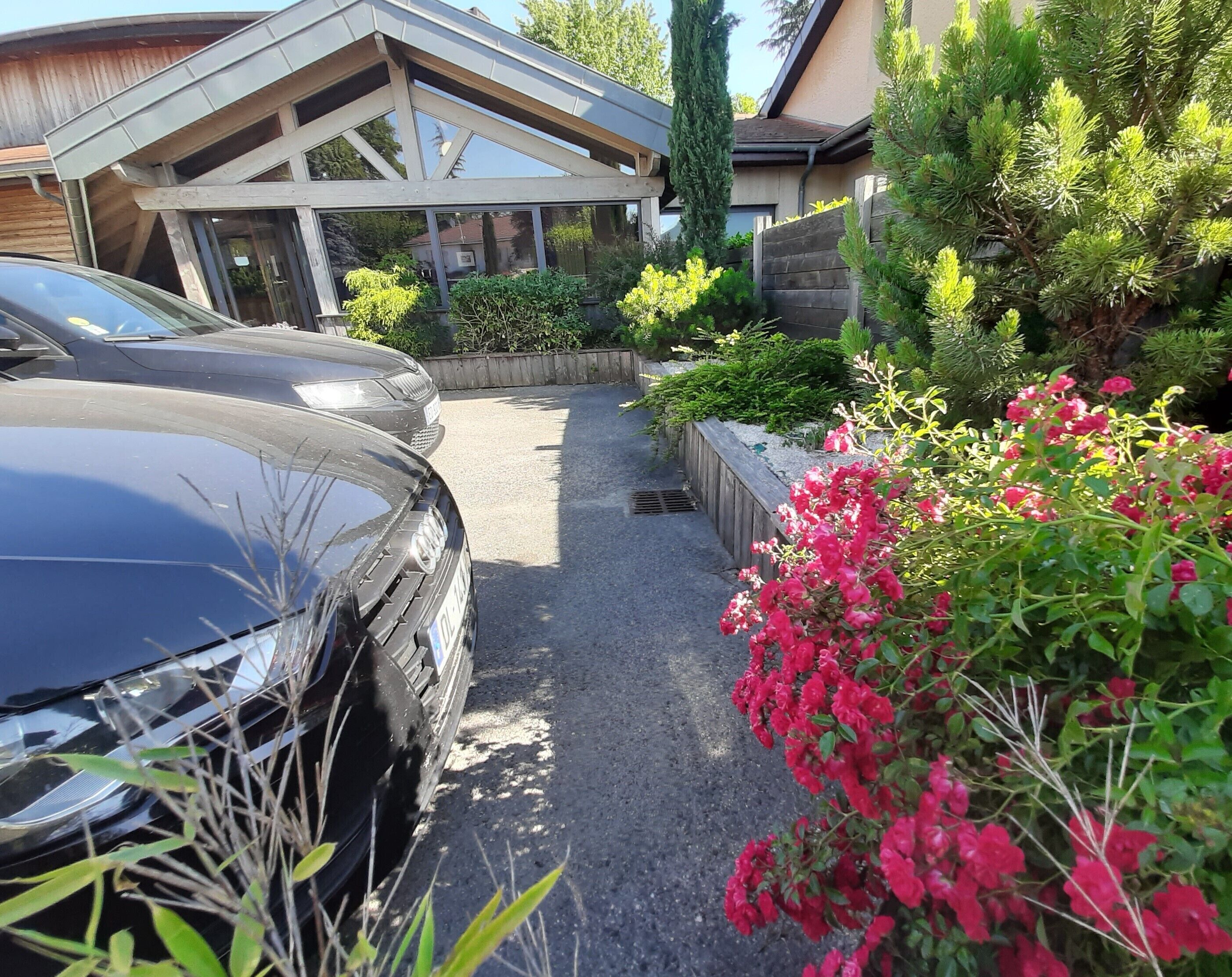 A modern house with a garage, parked cars, and a garden with pink flowers.