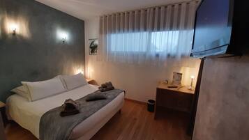 Una habitación de hotel moderna con cama, mesitas de noche, televisor y ventana con cortinas.
