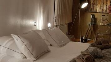 Et hotelværelse med en seng, puder, en sengetavlelampe, et glasbord og et håndklæde.