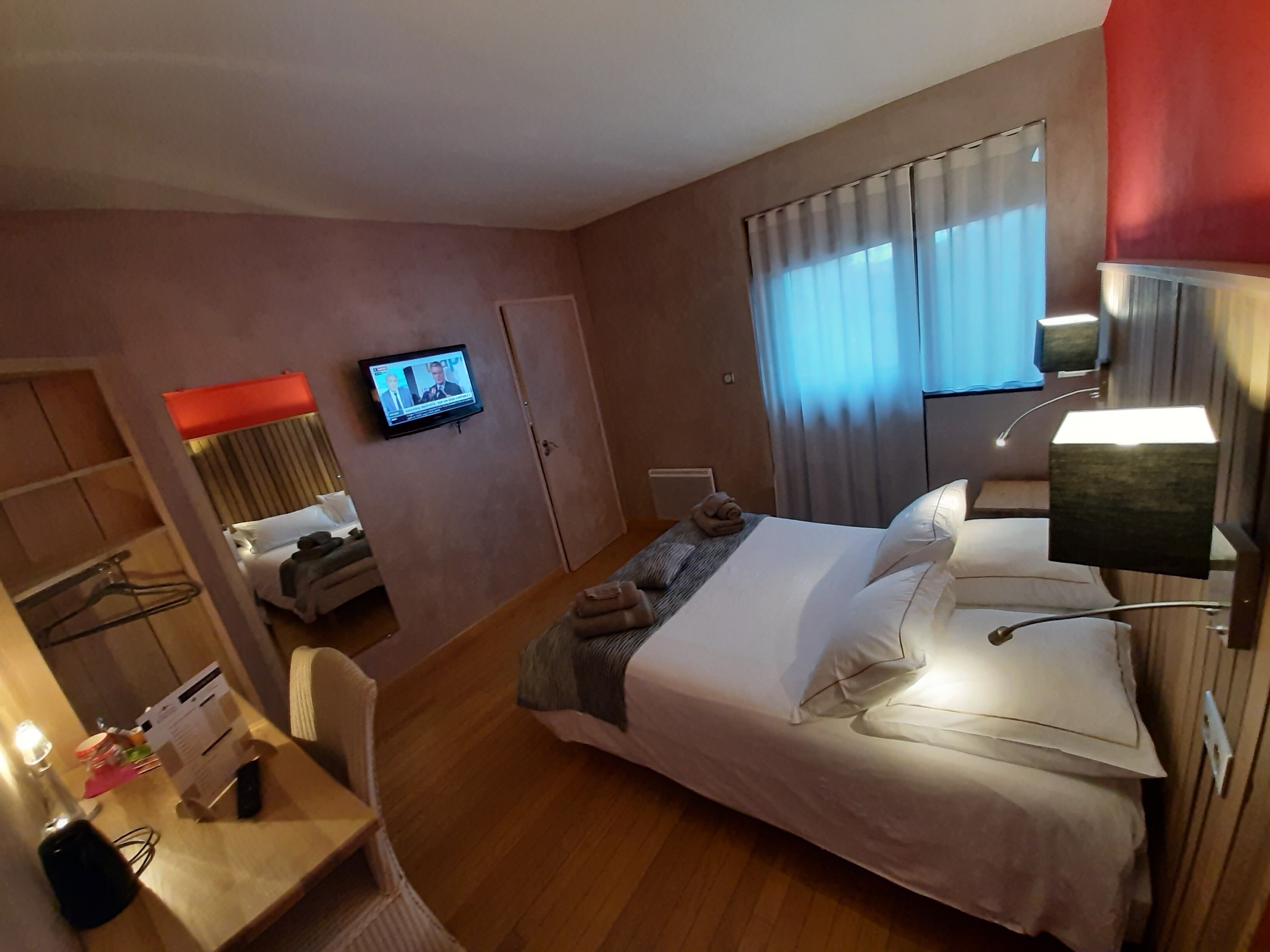Habitación de hotel con cama, escritorio, silla, televisor en la pared y ventana con cortinas.