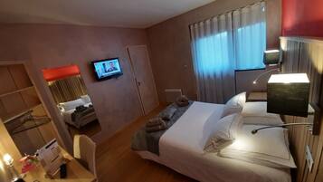Habitación de hotel con cama, escritorio, silla, televisor en la pared y ventana con cortinas.