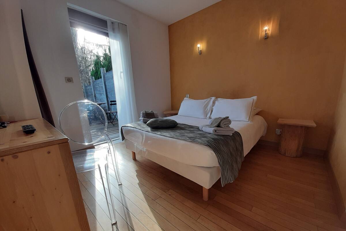 A bedroom with a bed, a wooden floor, a small wooden table, and a chair.