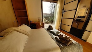 Habitación de hotel con cama, piso de madera, una mesita con lámpara y vista al exterior.