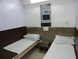A hotel room with two single beds, a small bedside table, a wall-mounted TV, and a power outlet.