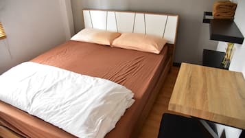 A neatly made bed with a white comforter and two pillows, a wooden bedside table, and a small black chair.