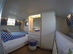 A compact bedroom with a bed, a dresser, a mirror, and a small stool.