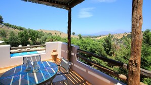 A terrace with a pool, table, and chairs, overlooking a hilly landscape. - Villa Dafni (Faistos)