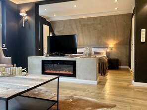 A modern hotel room with a fireplace, a flat-screen TV, a bed with a headboard, and a seating area with a table and chairs. - country-suites by verdino LIVING (Braunlage)