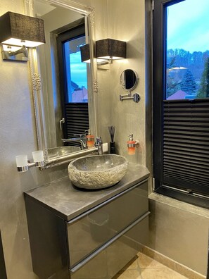 A modern bathroom with a large stone sink, a mirror with an ornate frame, and a window with blinds. - country-suites by verdino LIVING (Braunlage)