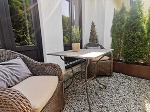 A wicker sofa and a small table with a cushion, set on a gravel floor with a view of greenery through large windows. - country-suites by verdino LIVING (Braunlage)