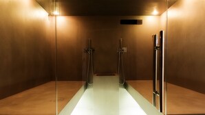 Casa de banho moderna com divisória de vidro, duas peças em cromo e iluminação quente.