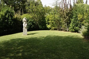 Escultura numa área gramada com árvores densas ao fundo.