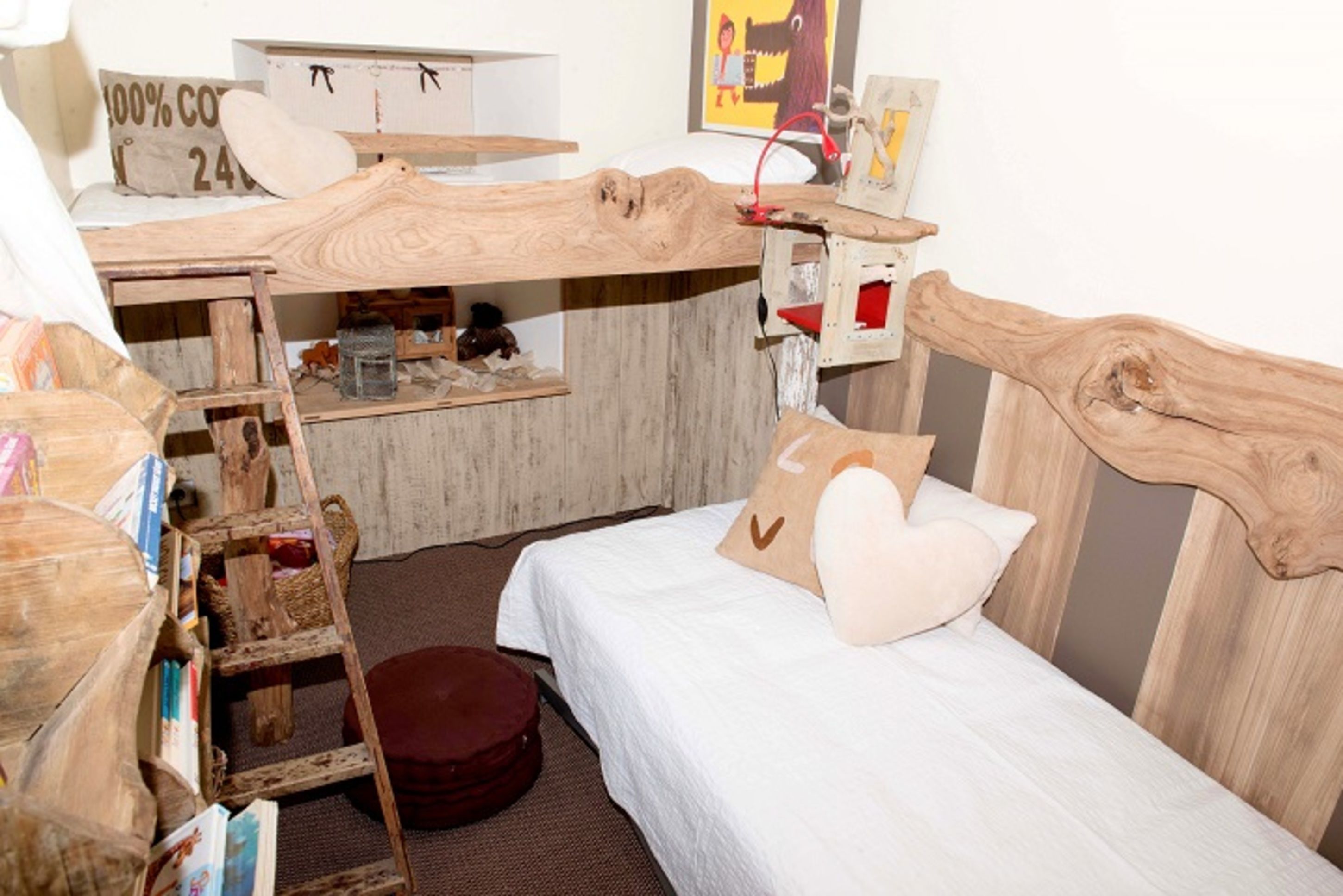 Una habitación con una cama nido de madera, un escritorio pequeño con una silla y una escalera. Hay una cama blanca con un almohadón y una alfombra redonda pequeña.