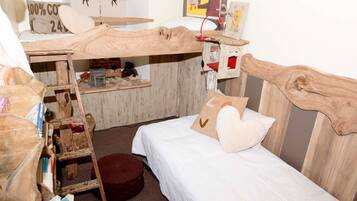 Una habitación con una cama nido de madera, un escritorio pequeño con una silla y una escalera. Hay una cama blanca con un almohadón y una alfombra redonda pequeña.